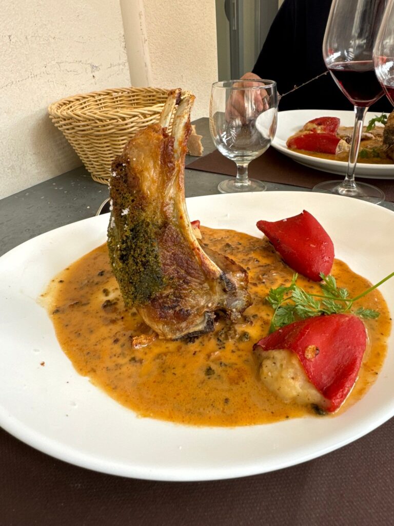 Succulente côte d'agneau rôtie à la croûte d'herbes, baignant dans une sauce riche, servie avec des poivrons rouges farcis. Scène de restaurant.