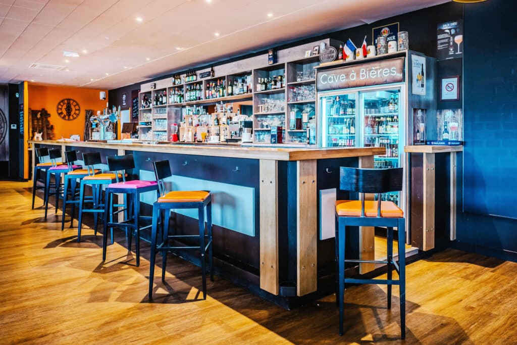 Bar moderne avec comptoir en bois, tabourets colorés et Cave à Bières lumineuse.