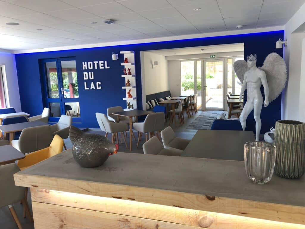 Intérieur moderne de l'Hôtel du Lac avec mur bleu, mobilier contemporain, étagères décoratives, et mannequin ange. Lumière bleue ambiante.