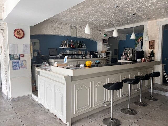 Intérieur de bar avec comptoir blanc sculpté, tabourets hauts noirs, luminaires suspendus et mur d'accent bleu.