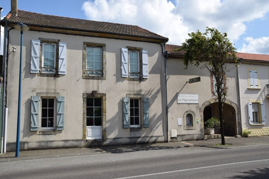 Façade du Restaurant Le Pigeonneau avec fenêtres aux volets bleus, entrée voûtée et arbre en face.
