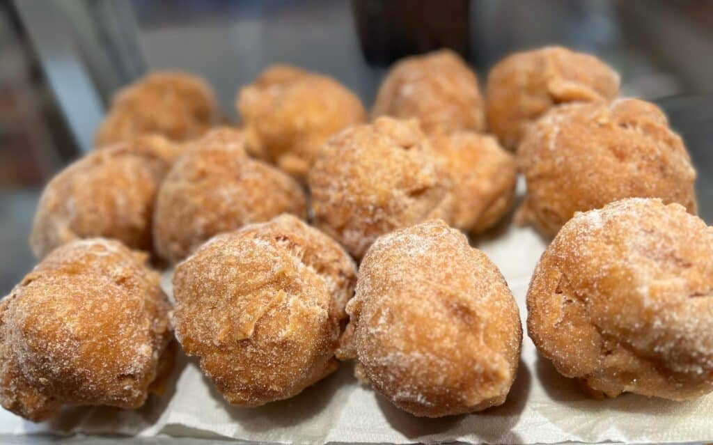 Pile de beignets ronds et dorés, généreusement saupoudrés de sucre blanc, sur un papier absorbant.