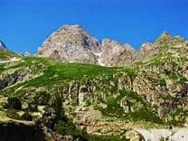 Vaste paysage alpin rocheux sous un ciel bleu éclatant. Pentes vertes luxuriantes et sommets majestueux en haute montagne.