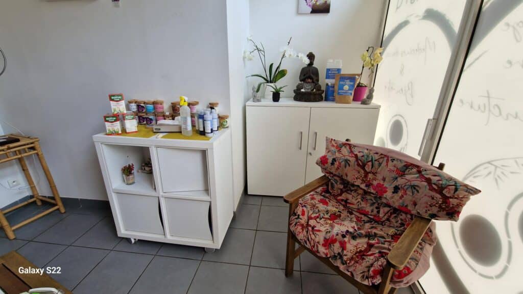 Espace bien-être lumineux avec produits naturels (Richter's, Casa Nature), fauteuil en bois à coussin floral, bouddha, orchidées et étagères blanches.
