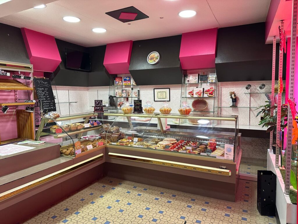 Boulangerie-pâtisserie moderne rose et noir. Vitrines de gâteaux, tartes, pains, viennoiseries. Menu Pizza: Marguerite 9€, Chèvre 9€...