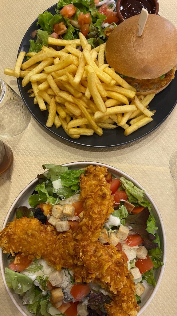 Burger, frites dorées et petite salade sur assiette noire. Grand bol de salade fraîche avec tenders de poulet croustillants et croûtons.
