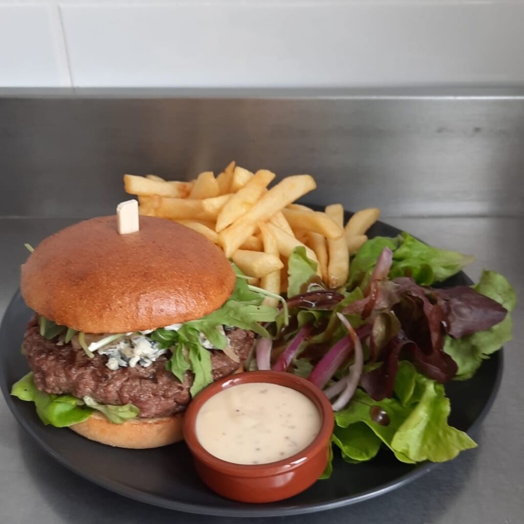 Délicieux burger au bœuf, fromage bleu et roquette, accompagné de frites dorées croustillantes et d'une salade fraîche avec sauce.