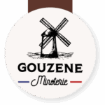 Logo circulaire Gouzene Minoterie: un moulin à vent traditionnel dessiné en noir, surmontant les mots 'GOUZENE Minoterie' encadrés de traits bleu et rouge.