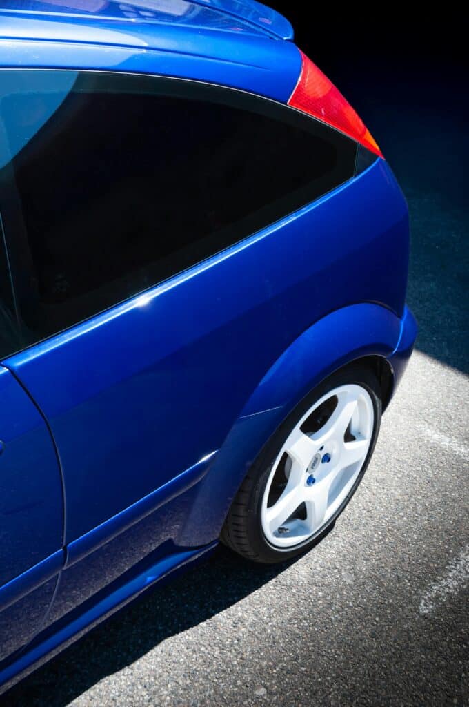 Close-up of a blue sports car with white rims shining in sunlight, outdoors.