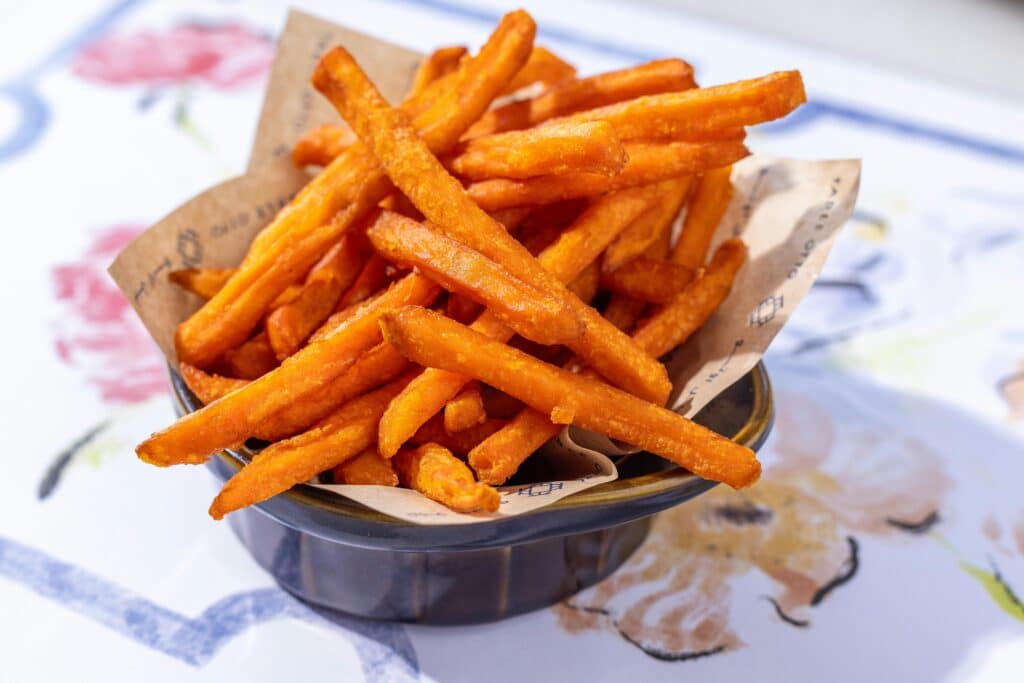 A bowl of crispy sweet potato fries served on an artistic table setting, perfect for food lovers.