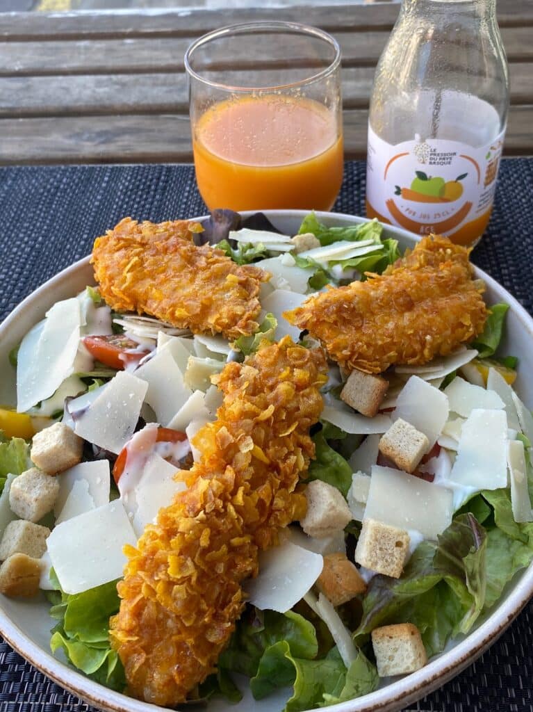 Salade César avec poulet croustillant, parmesan, croûtons. À côté, un verre de jus ACE 