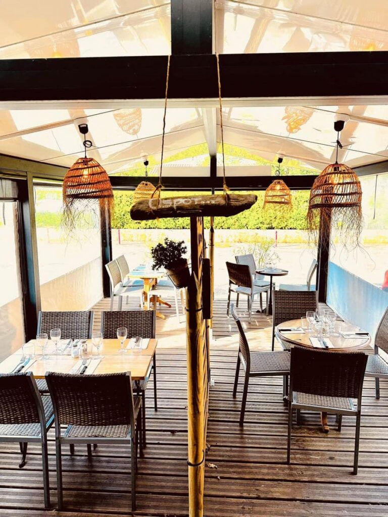 Terrasse de restaurant en bois avec tables dressées et chaises tressées. Luminaires bohèmes en osier et élément 