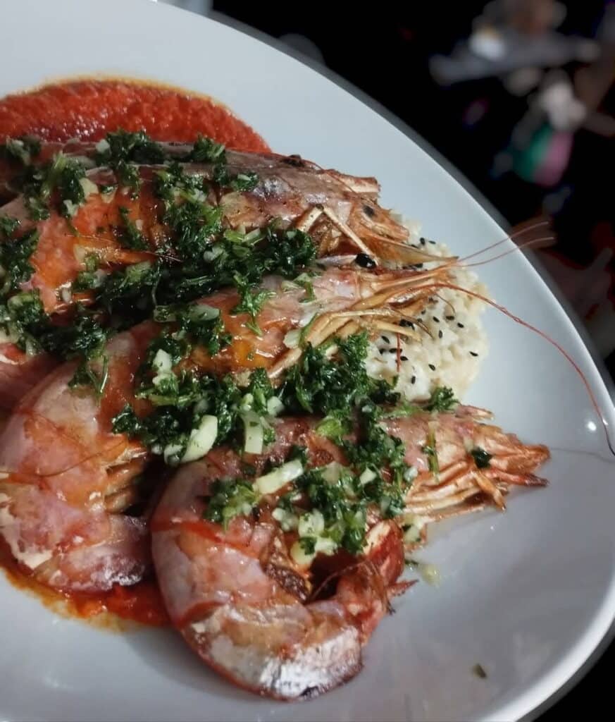 Grosses crevettes décortiquées et grillées, garnies d'ail et de persil, servies sur un lit de risotto crémeux avec une sauce tomate.