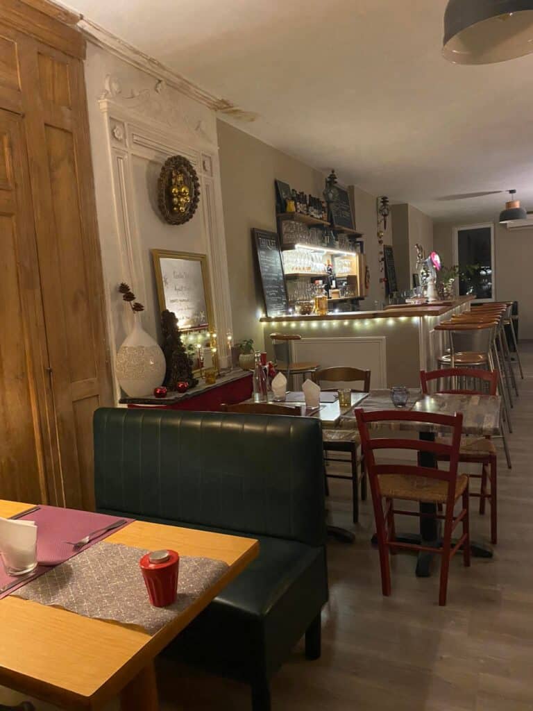 Intérieur chaleureux d'un restaurant avec un coin salon banquet vert, des tables dressées et un bar illuminé avec tabourets hauts.