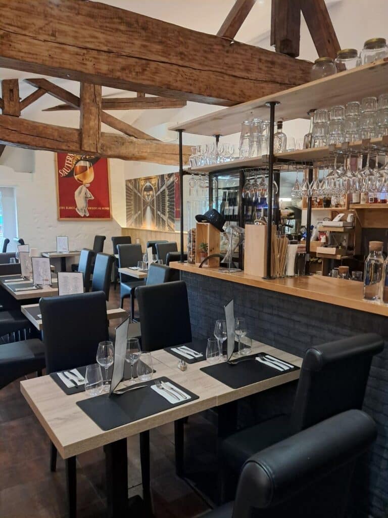 Intérieur restaurant chic avec poutres apparentes, tables dressées et bar moderne. Affiche Sauternes et cave à vin.