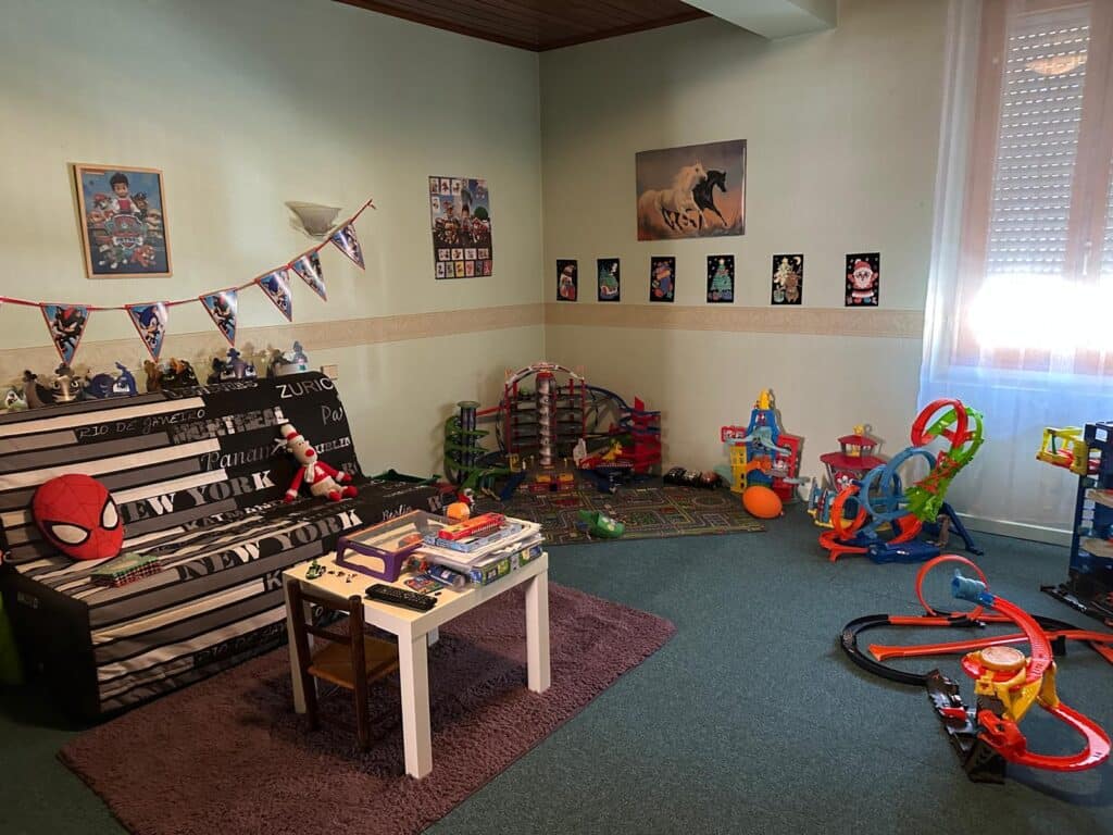 Chambre d'enfant remplie de jouets : circuits de voitures Hot Wheels, canapé décoré de 'NEW YORK', posters Paw Patrol et Sonic.