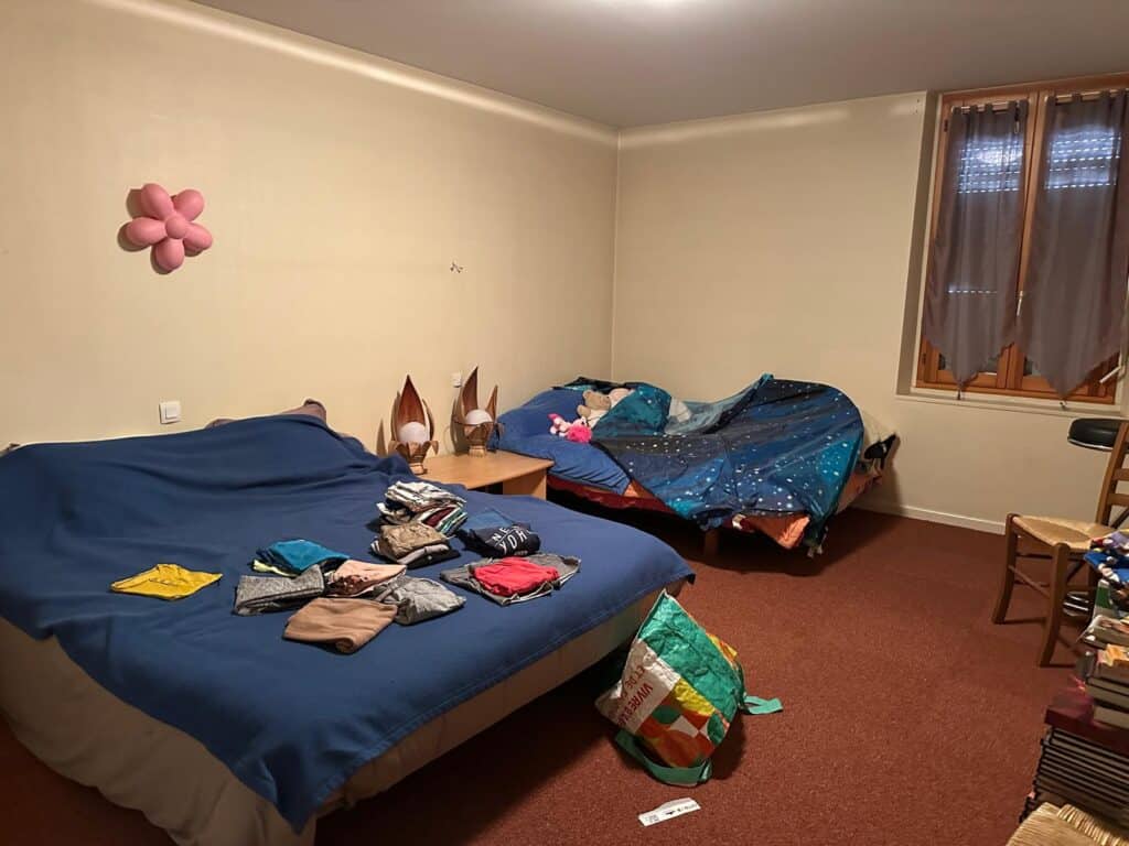 Chambre avec deux lits, un grand bleu avec des vêtements pliés et un plus petit sous couette galaxie. Sac réutilisable 