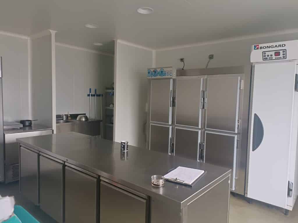 Cuisine professionnelle inox avec îlot central, réfrigérateurs BONGARD et panneau de contrôle Panamatic, matériel propre.