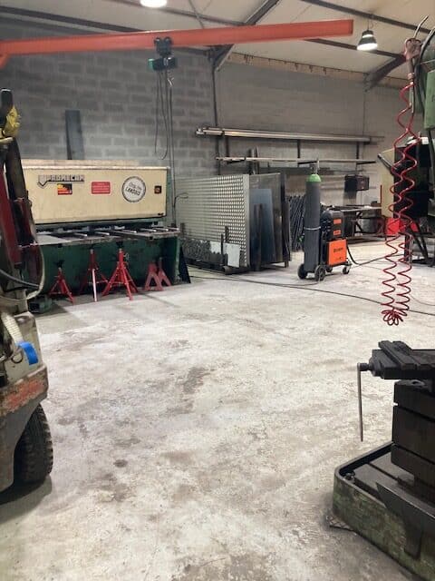 Atelier de métallurgie propre avec cisaille PROMEÇAM, stock de tôles d'acier et poste de soudure mobile. Pont roulant visible.