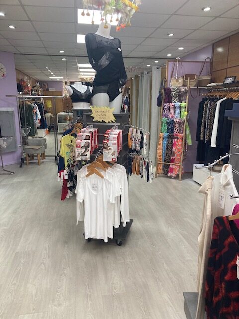 Boutique de mode avec lingerie, t-shirts blancs et signe 'Nouveauté Culotte Coton' sur un présentoir central.