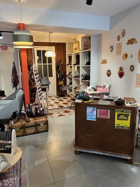 Boutique de mode vintage avec comptoir en bois, étagères de chaussures et affiche Vide-grenier 15 mars 2026.