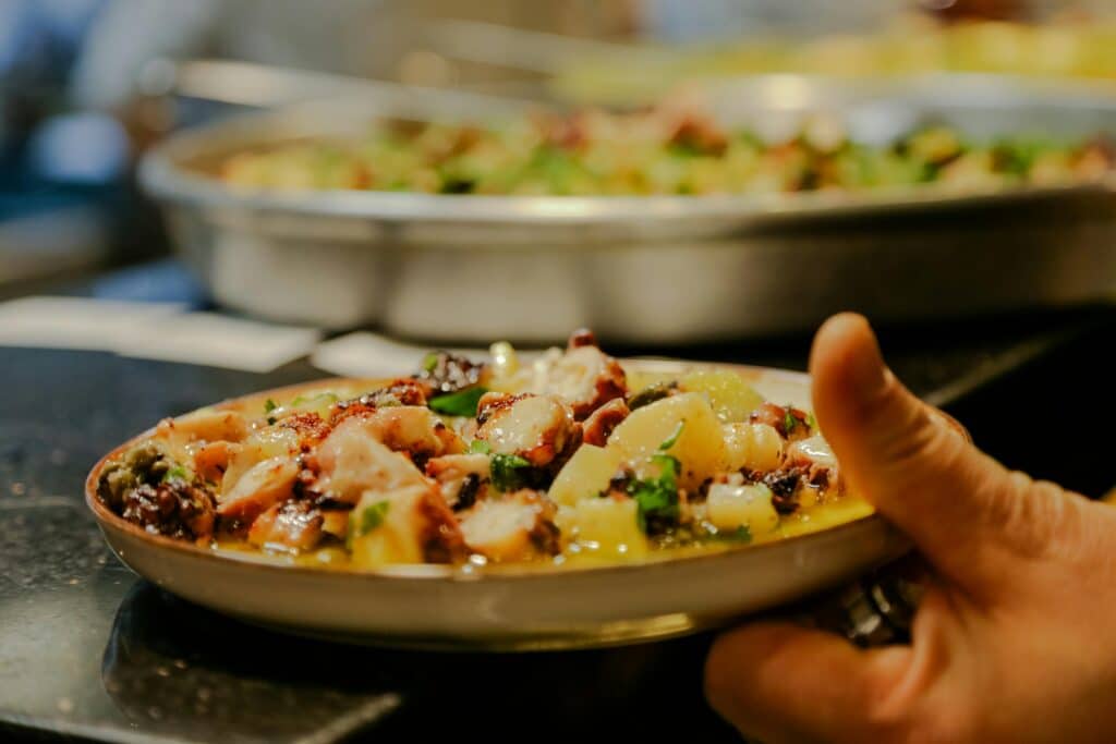 A vibrant dish of octopus and potatoes garnished with herbs, presented on a ceramic plate.