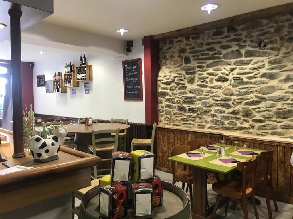 Salle de restaurant rustique avec mur en pierre apparente, menu du jour à l'ardoise et mobilier en bois chaleureux.