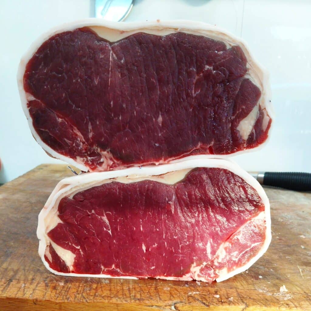 Deux pièces de bœuf cru à chair rouge sombre bardées de gras blanc sur un billot de bois de boucherie.
