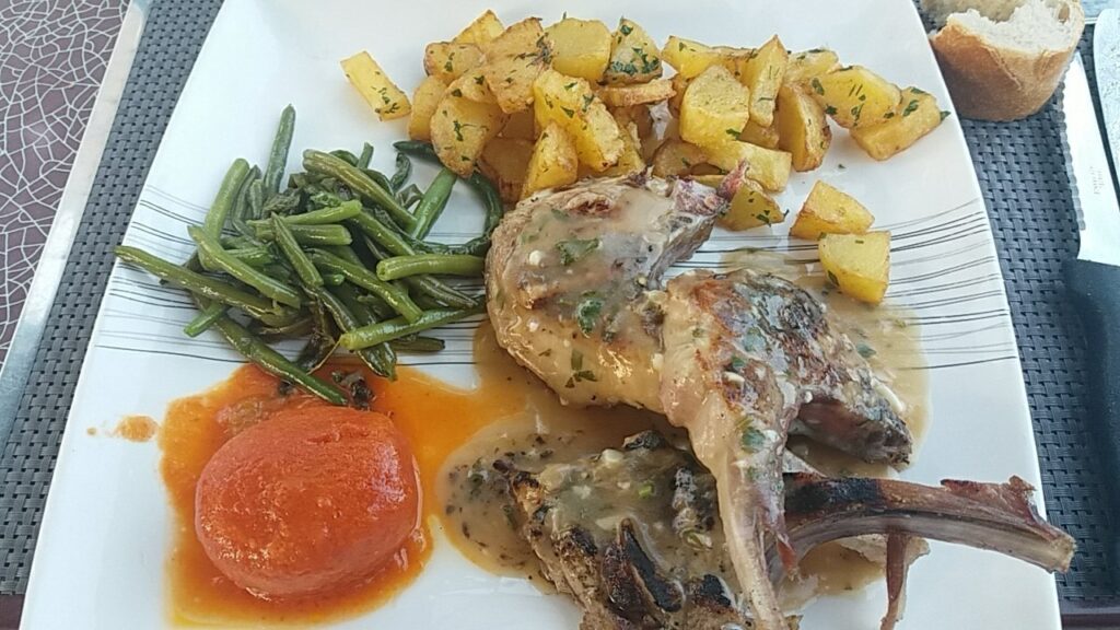 Côtelettes d'agneau en sauce, pommes rissolées aux herbes, haricots verts et tomate rôtie.