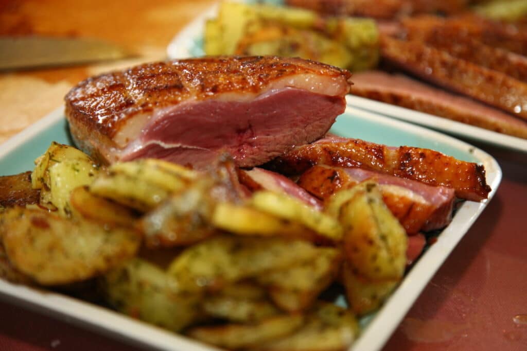Magret de canard rôti rosé et pommes de terre grenailles aux herbes sur un plat.