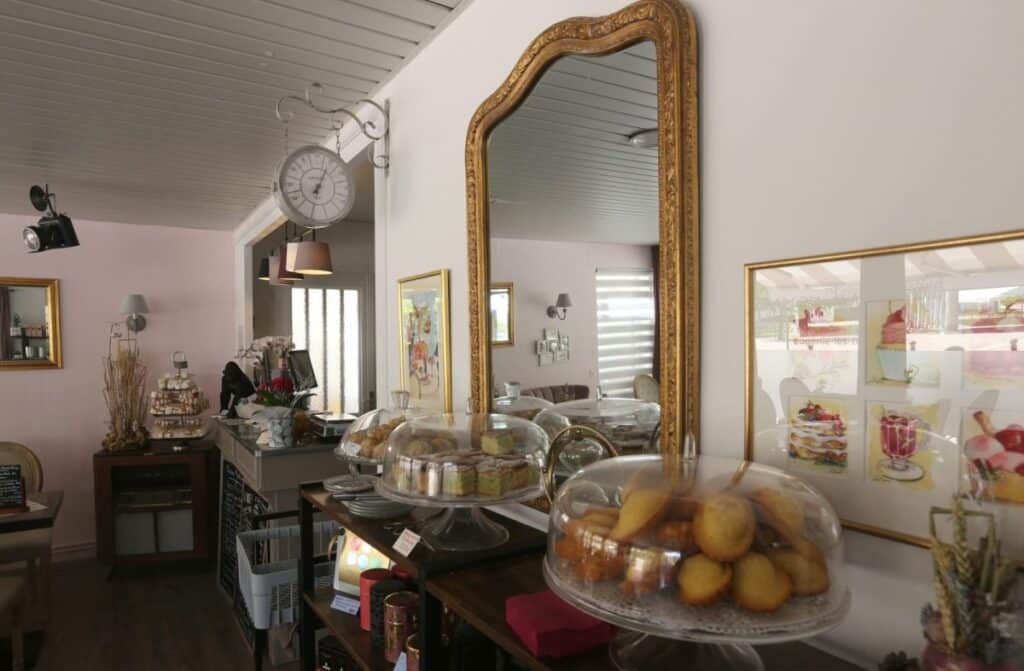Intérieur d'une pâtisserie élégante avec gâteaux sous cloche et grand miroir doré.