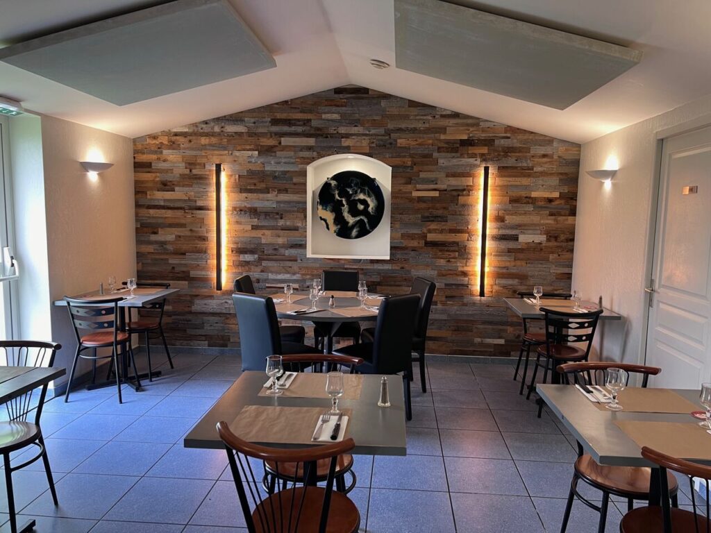 Salle de restaurant moderne avec mur en bois, tables dressées et éclairage chaleureux.