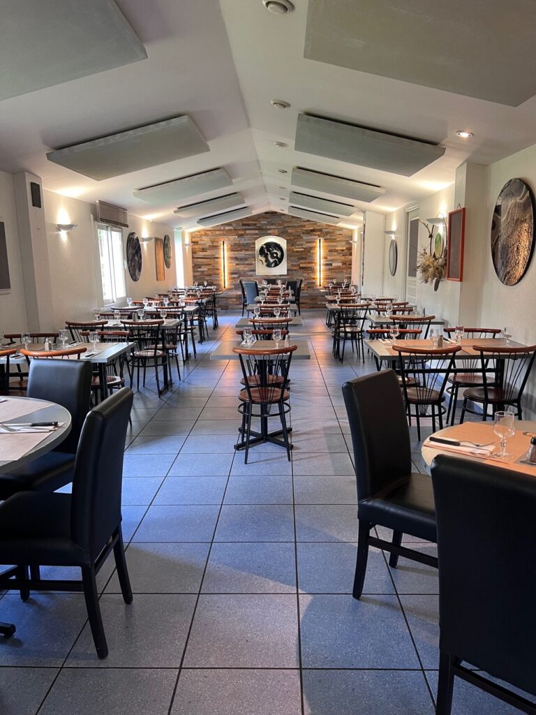 Salle de restaurant moderne avec tables dressées, chaises en bois et mur de fond boisé décoratif.