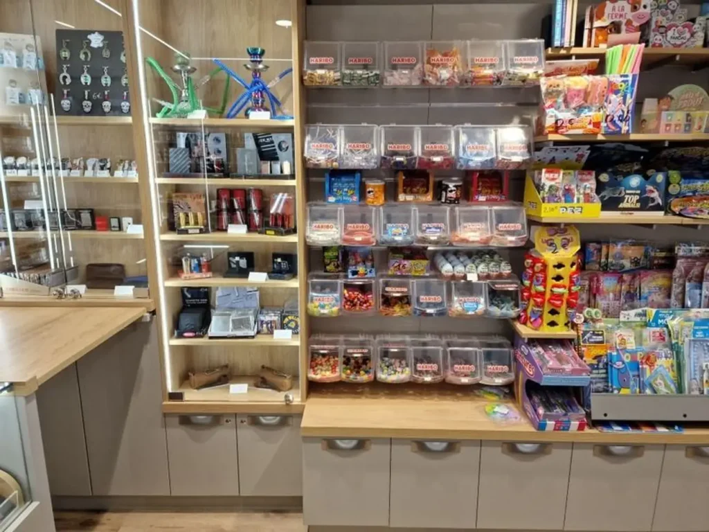 Rayonnages de magasin avec narguilés, briquets, bacs de bonbons Haribo et jouets colorés pour enfants.