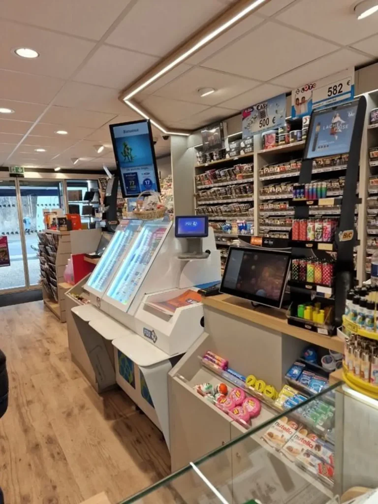 Intérieur de tabac presse avec terminaux FDJ Loto, étagères de cigarettes, briquets Bic et confiseries au comptoir.