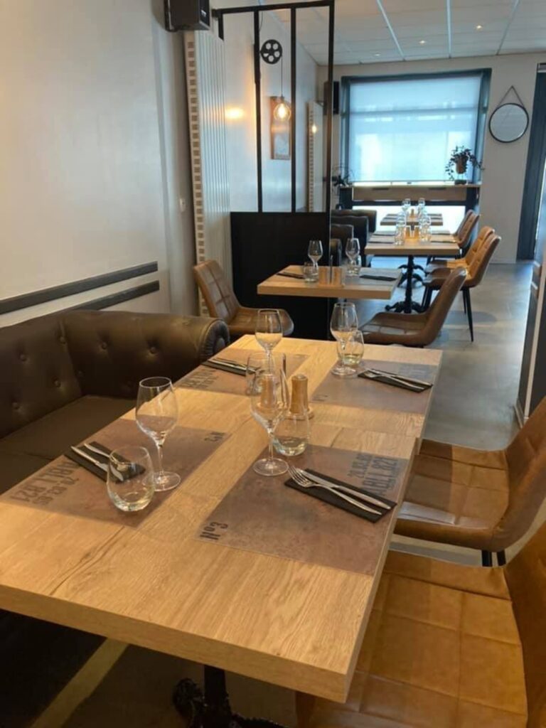Salle de restaurant moderne avec tables en bois, chaises en cuir marron et verres à pied dressés.